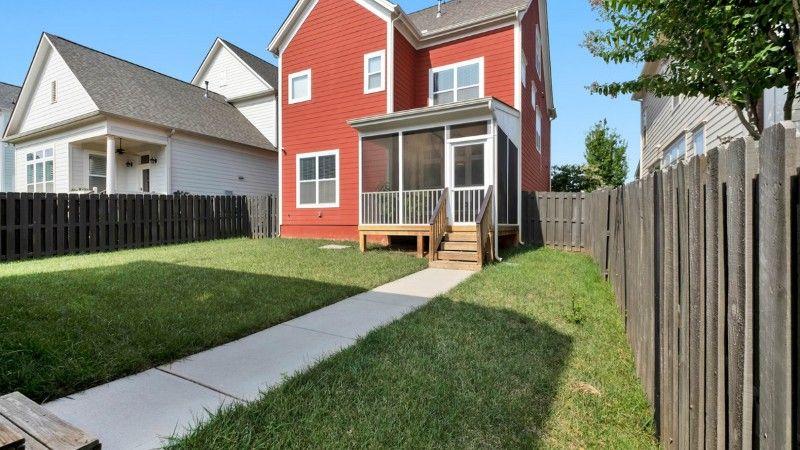 Backyard lawn between two houses with partial sunlight and shade along the fence.