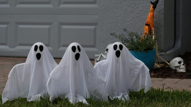 Three ghost decorations made with white sheets stand on a front lawn, adding spooky charm for Halloween.