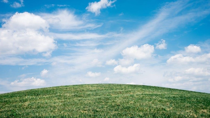 A gently sloped green lawn under a bright blue sky with scattered white clouds, symbolizing eco-friendly yard care.
