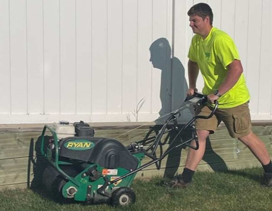 Green Drop technician operating a core aerator beside a residential fence