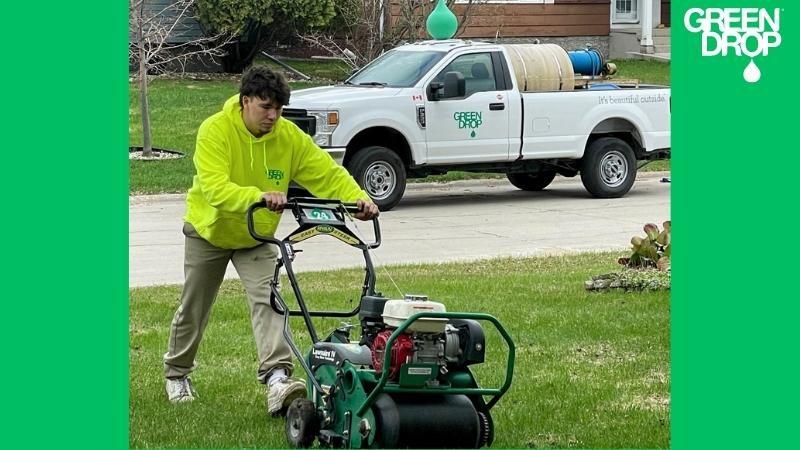 Green Drop technician aerating a residential lawn beside a service truck