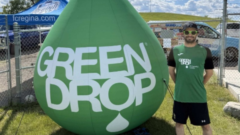 Green Drop team member standing beside a large branded display at the 2026 FC Regina Summer Fest.