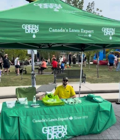 Green Drop representative seated at a branded community event booth with families and visitors in the background.
