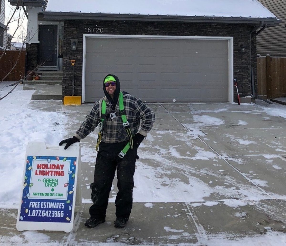 A Green Drop employee standing in front of a house with a sign for holiday lighting
