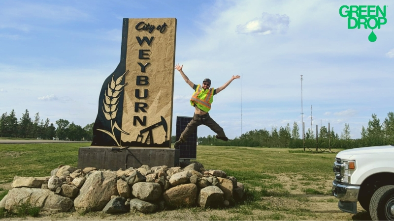 Green Drop tree worker jumping in front of a Weyburn city sign