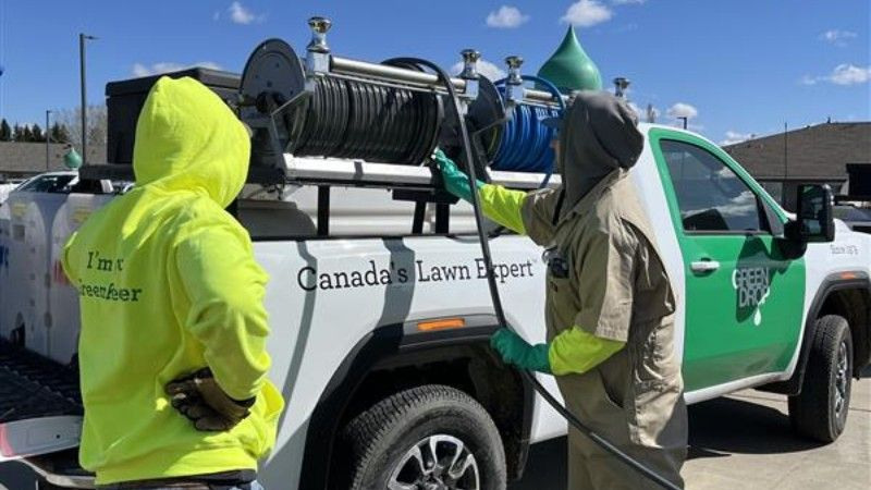 Two Green Drop technicians standing beside a branded truck, prepping hose equipment for lawn service