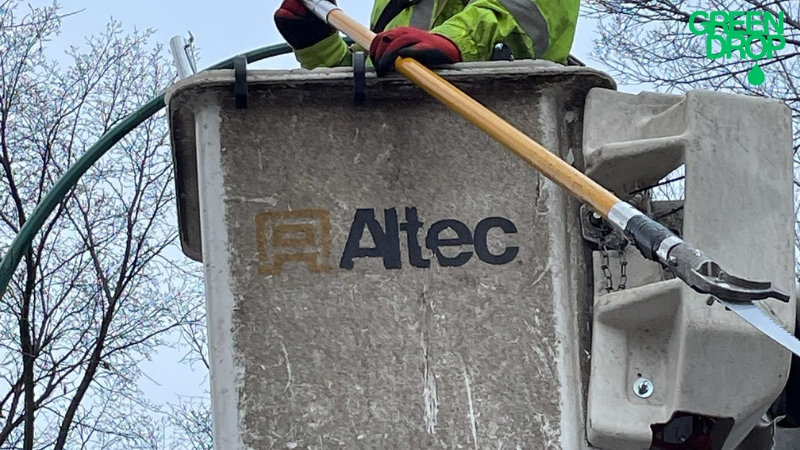 Green Drop worker cutting a tree while on a lift