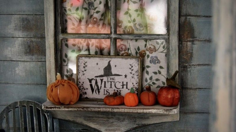 A rustic Halloween window decorated with small pumpkins and a sign reading “The Witch is In.”