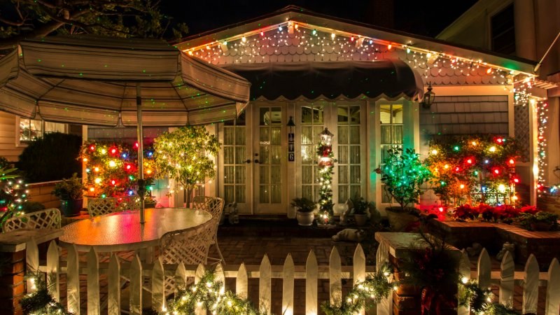 House porch and garden with a picket fence decorated with holiday lights at night