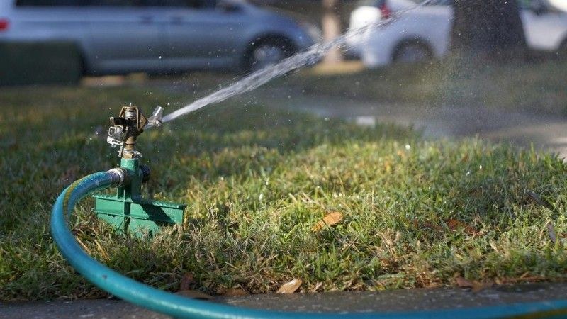 Close-up of a sprinkler spraying water across the grass using a hose connection