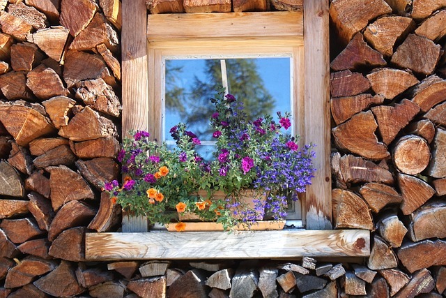 A pile of firewood with a window in the middle and flowers