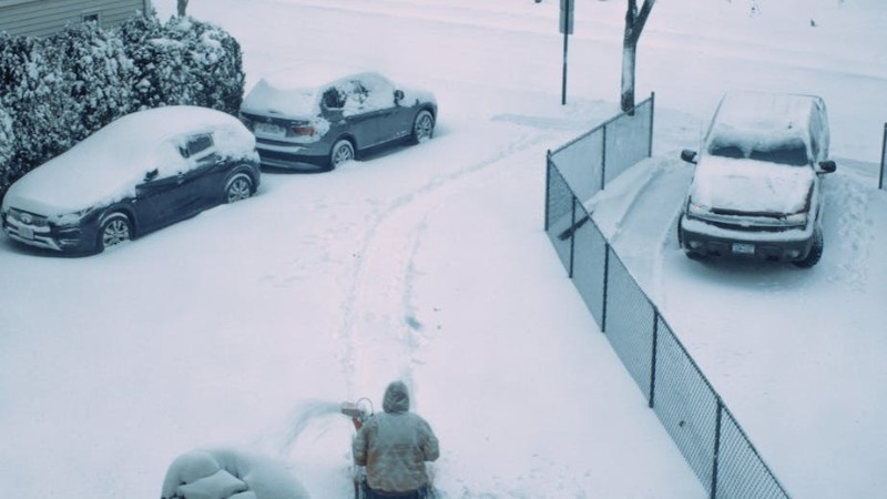 Person using a snowblower to clear a driveway covered in fresh snow, illustrating a safer alternative to manual shovelling.