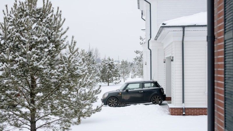 A snow-covered driveway beside a modern white house with a parked car, representing the need for regular snow clearing during winter.