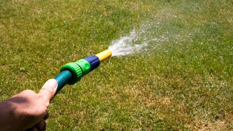 Garden hose spraying water across a patchy green and brown lawn