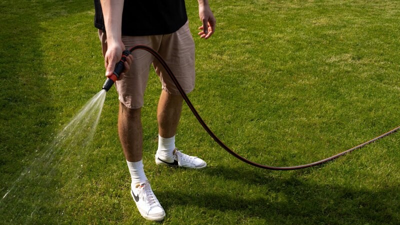 Man in white sneakers watering the grass